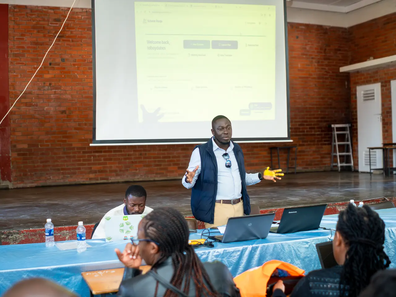 A Scheme Rangu facilitator in a navy vest demonstrating the platform in Mutare